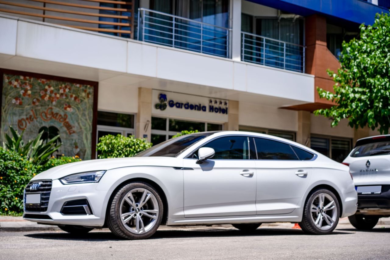 about-us White luxury car parked in front of a hotel with modern architecture.