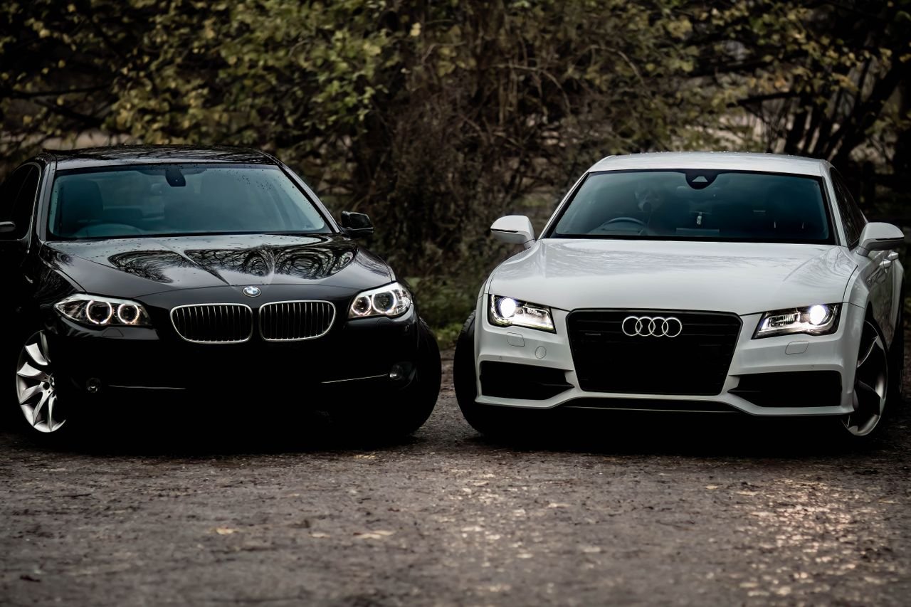 services-06 Black BMW and white Audi luxury sedans parked outdoors on a gravel path.